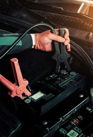 Ein Mitarbeiter mit Handschuhe schließt Starterkabel an einer Batterie an.