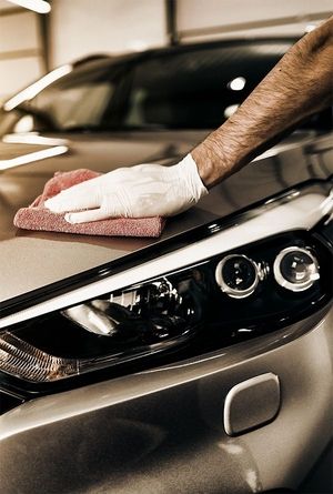 Ein Mann mit Handschuhe poliert die Motorhaube eines Autos.